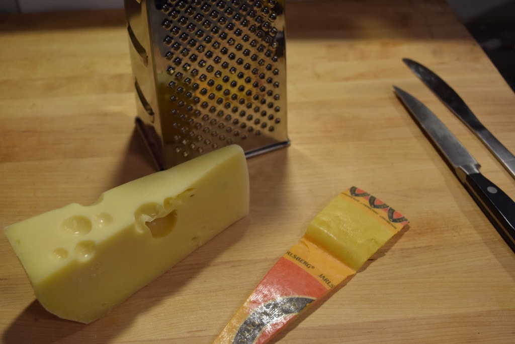 A wedge of Jarlsberg cheese next to a cheese grater.