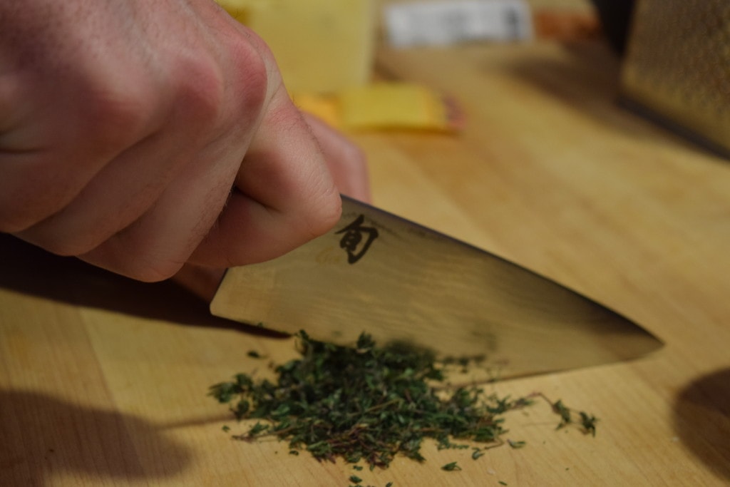 Shun knife chopping fresh thyme on a cutting board.