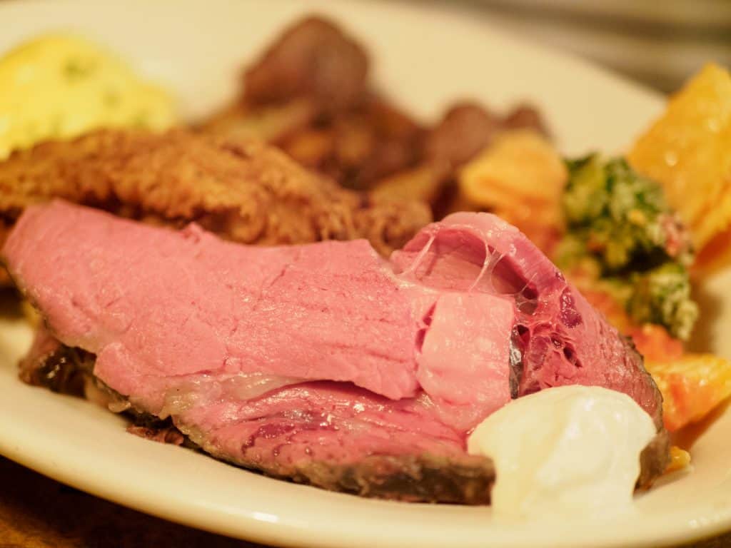 Medium rare prime rib on a plate with fried chicken.