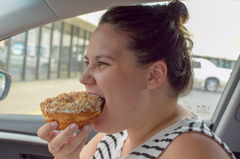 Woman eating iced donut from Kelly's Bakery Donuts & More in her car.