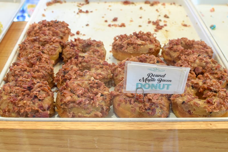 Donuts topped with maple icing and bacon on a bakery rack for sale at Holtman's donuts.