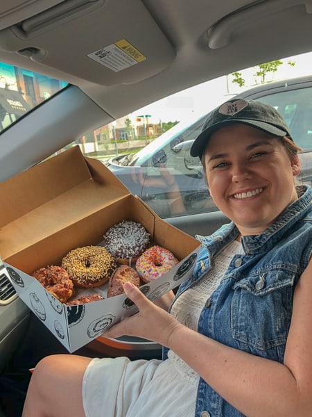 Woman smiling and holding a box of donuts from Holtman's donuts.