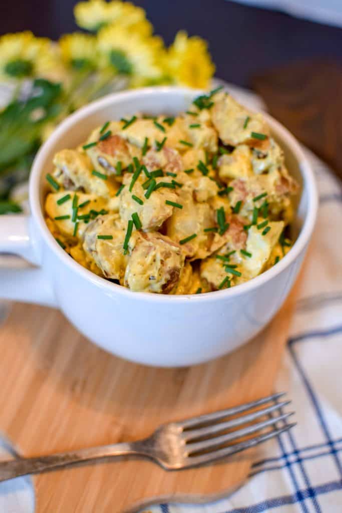 Red Skinned Potato Salad in a white serving dish on a wooden tray with a fork next to the bowl.