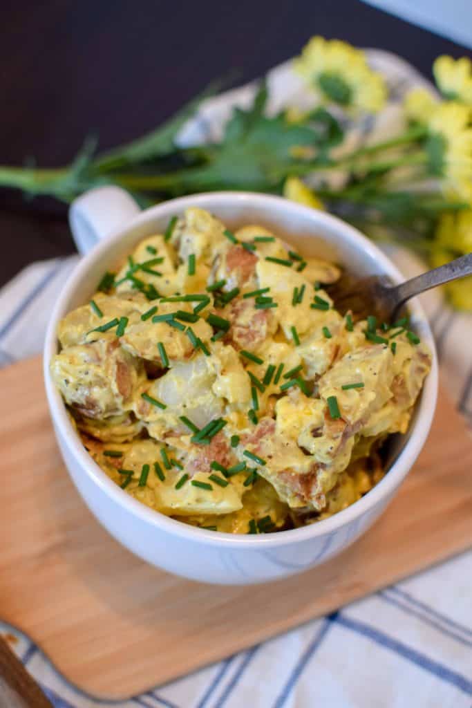 Midwest Red Skinned Potato Salad in a white serving dish with a fork scooping some out and fresh spring flowers in the background.