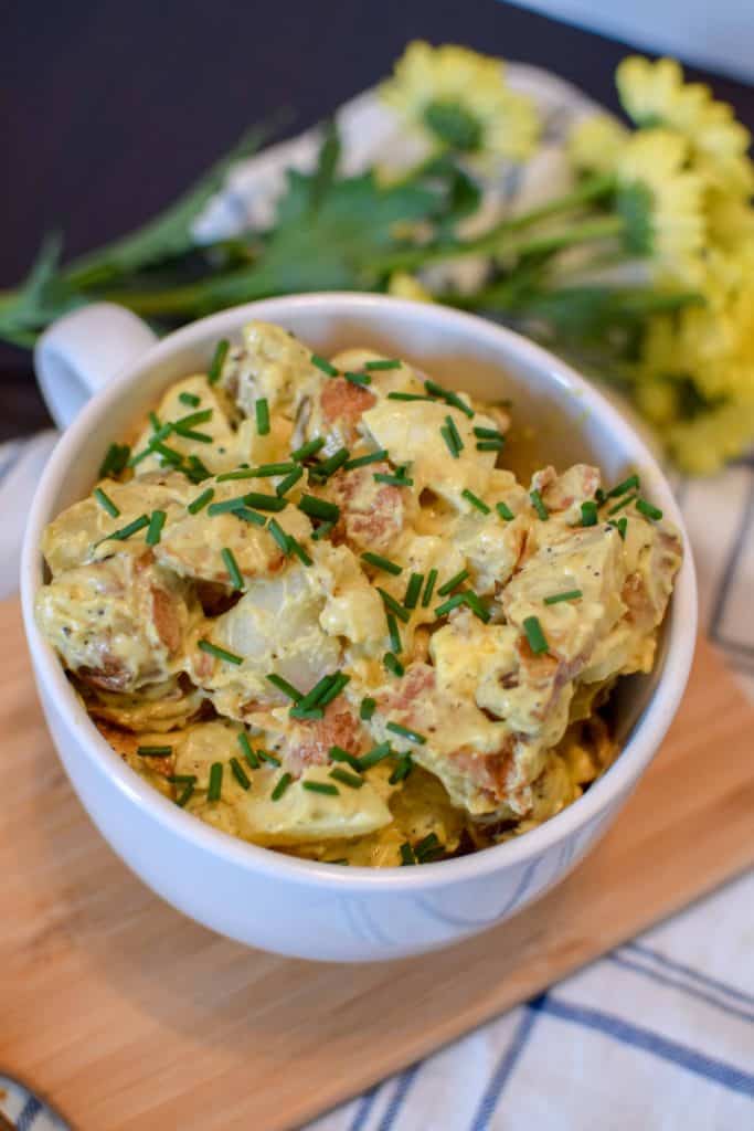 Red Skinned Potato Salad in a white serving bowl with fresh yellow flowers in the background.