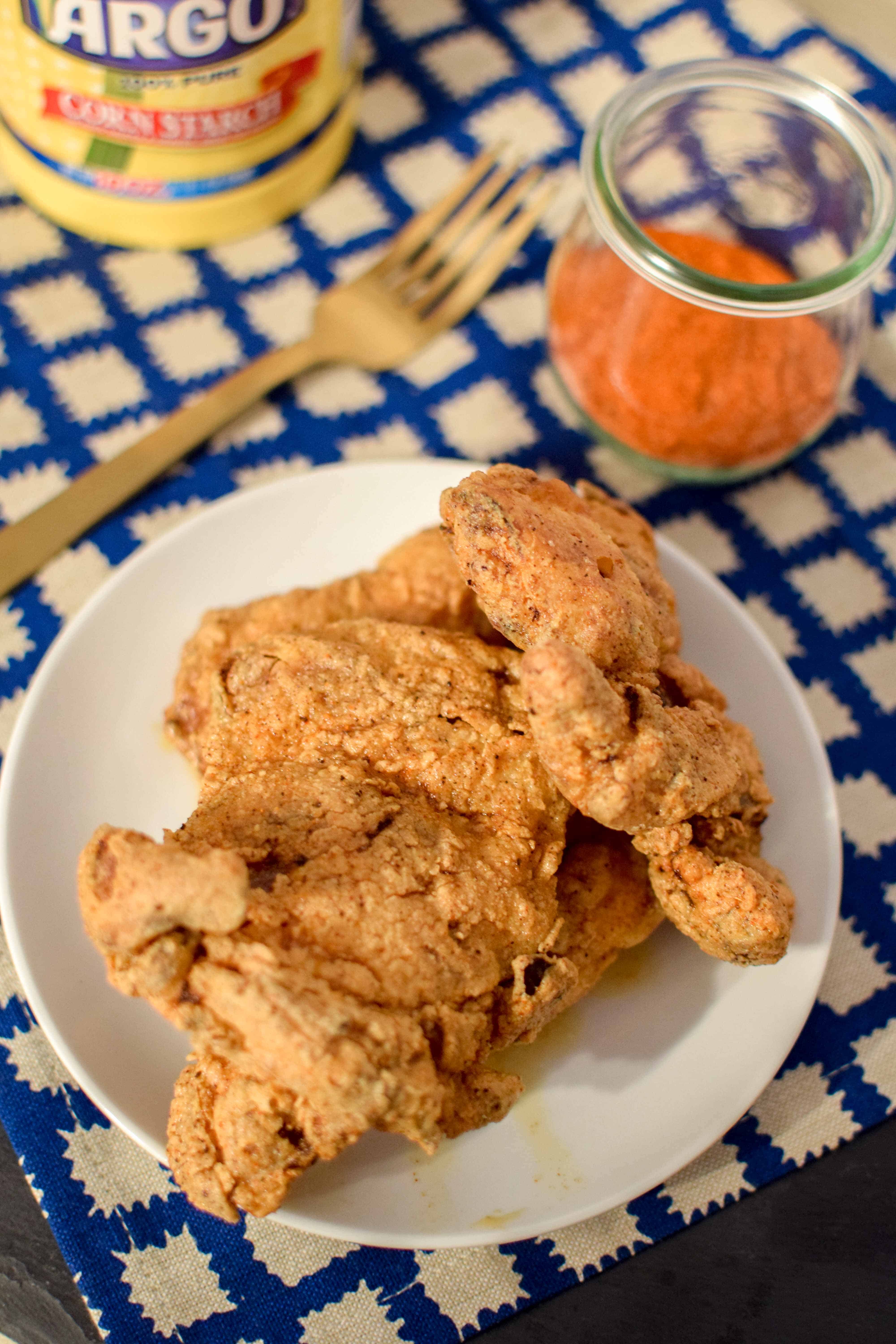 Crispy Nashville hot chicken thighs on a white plate over a blue and white tablecloth. 