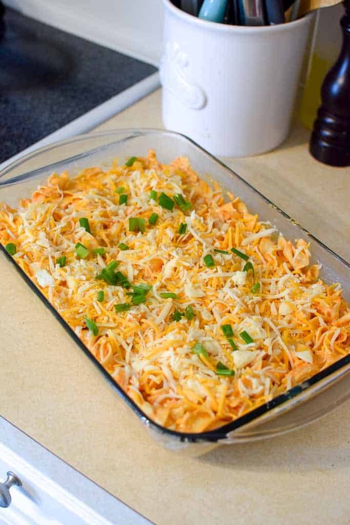 Midwest buffalo chicken casserole in a 9 by 13 glass baking dish sitting on a kitchen counter and topped with chopped green onions.