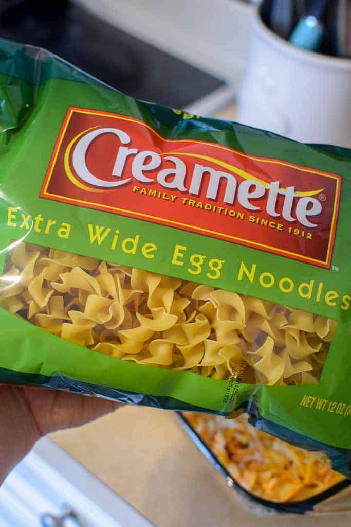 Hand holding a bag of Creamette extra wide egg noodles at home preparing to create a classic midwest buffalo chicken casserole. 