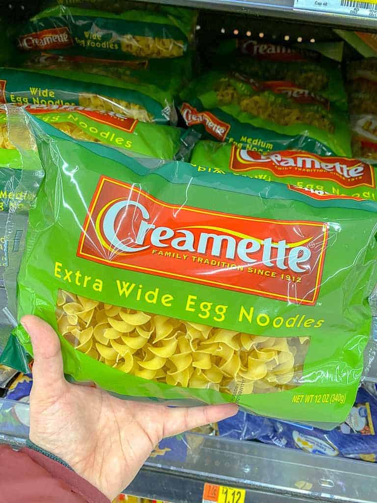 Customer holding a bag of Creamette extra wide egg noodles at the grocery store.