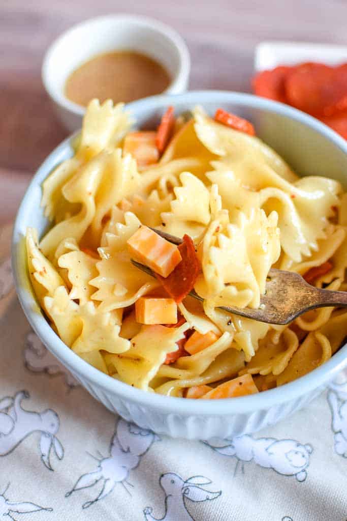 Close up of Classic Pasta Salad with cubed cheese, bowtie pasta, and pepperoni in a bowl on an easter dish towel with a side of dressing in the background.