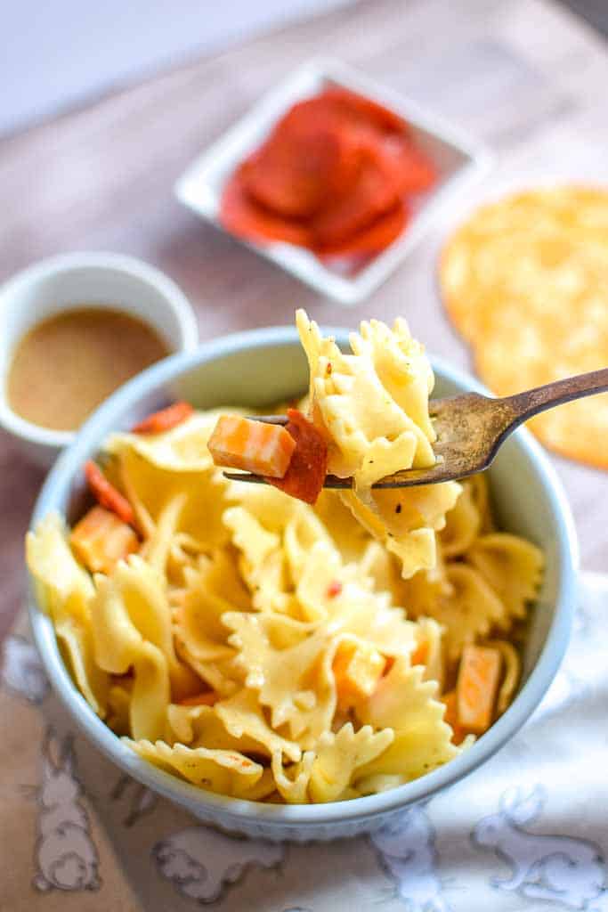 Scoop of pasta salad on a fork featuring cubed cheese, bowtie pasta, and pepperoni.