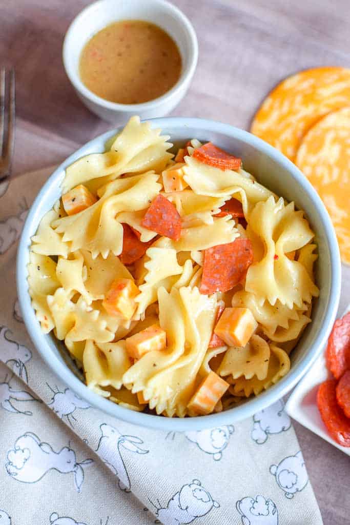 4 ingredient Pasta Salad shown in a bowl with a side dish of pepperoni and slices of colby jack cheese beside the bowl.