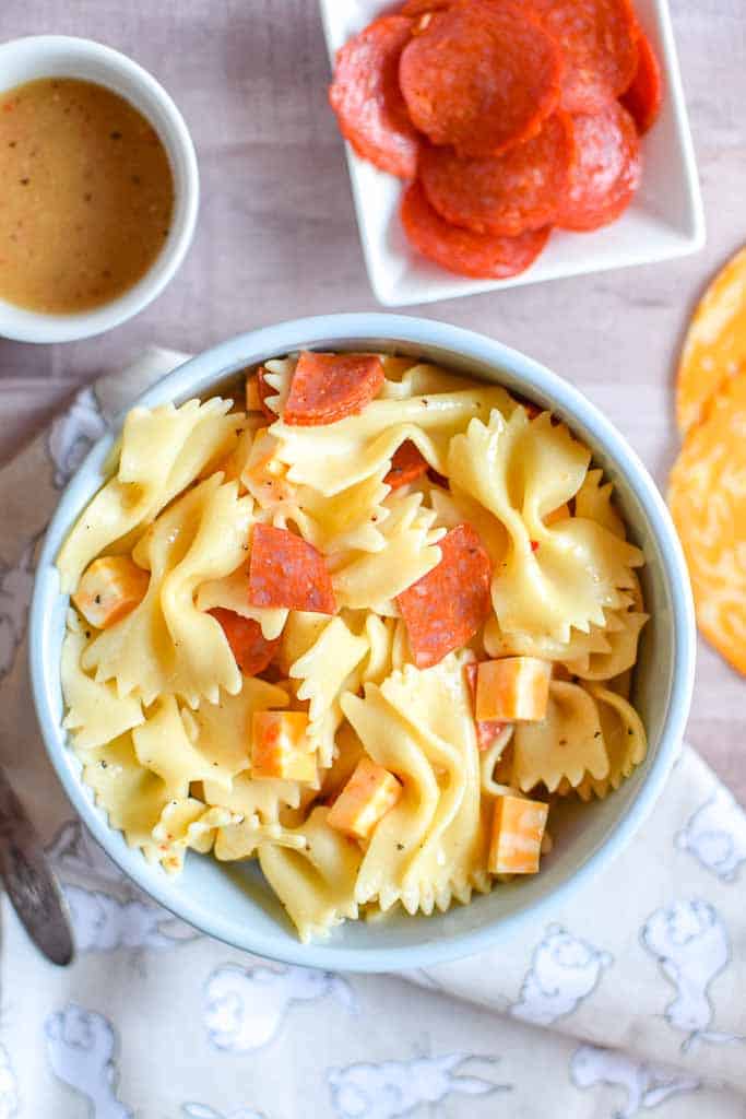 Classic Pasta Salad shown in a bowl with a side dish of pepperoni and a cup of dressing.