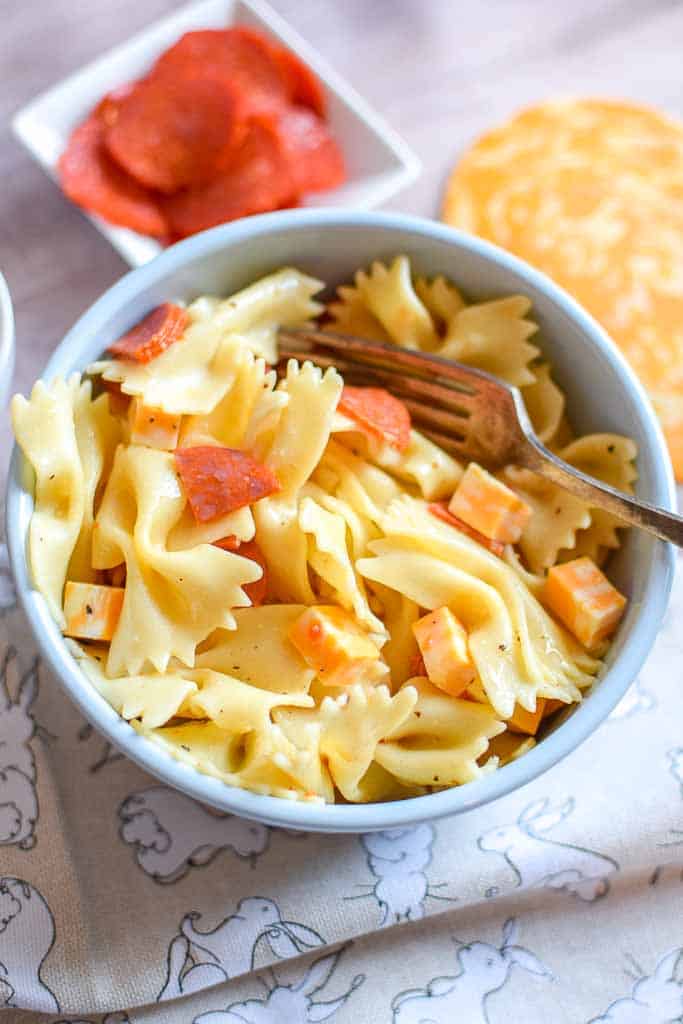4 ingredient Pasta Salad shown in a bowl with a side dish of pepperoni and slices of colby jack cheese beside the bowl.
