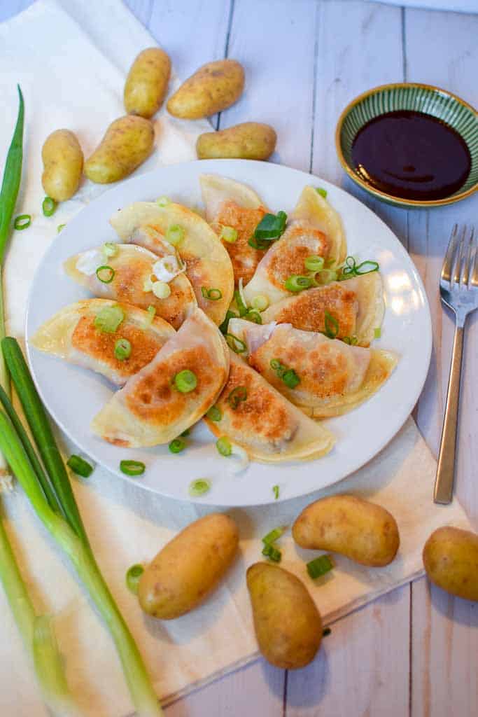 A white plate filled with corned beef dumplings with fingerling potatoes, a dipping cup of bbq sauce, and a fork next to the plate.