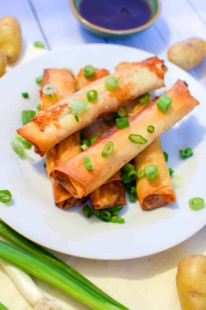 A white dish filled with stacked corned beef spring rolls in front of a cup of homemade Guinness barbecue sauce.