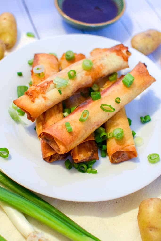 A white dish filled with stacked corned beef spring rolls in front of a cup of homemade Guinness barbecue sauce.