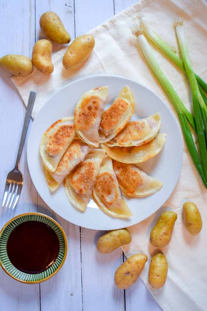 Overhead image of a white plate filled with corned beef dumplings surrounded by fingerling potatoes, whole green onions, and a dish of Guinness stout barbecue sauce.