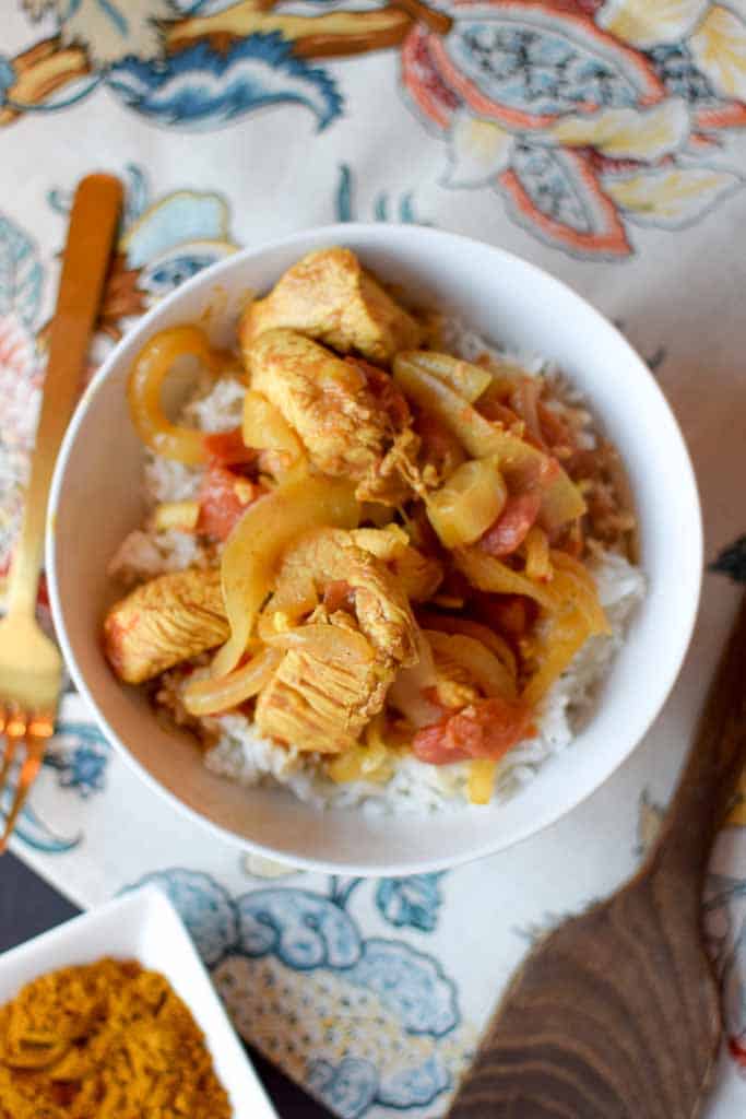 Chicken curry with veggies over rice in a white bowl.