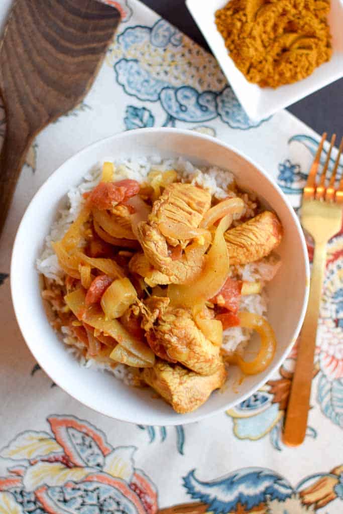 Chicken curry over rice in a bowl next to a gold fork.