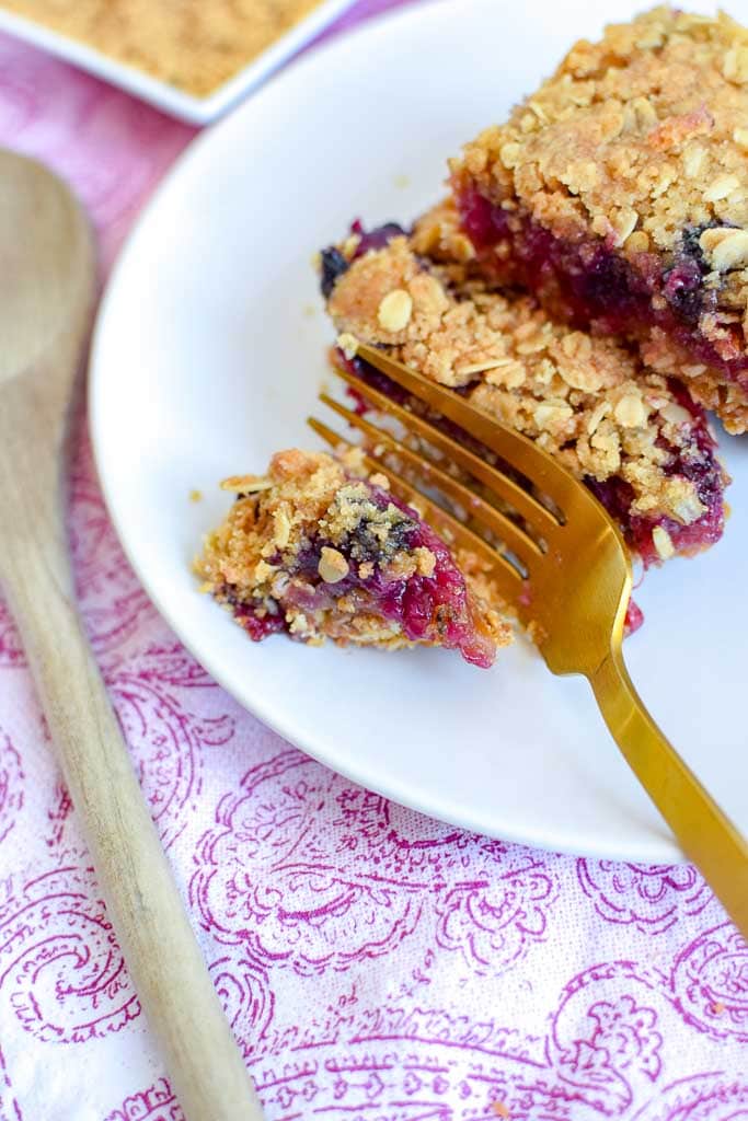 Golden fork cutting into Berry, Rhubarb, and Oat Breakfast Bars on a white plate.