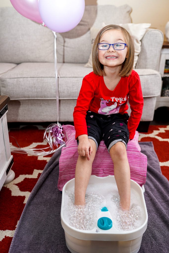 Child smiling while enjoying pedicure and foot spa at home.