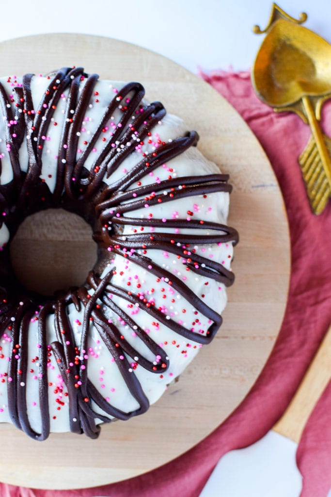 Overhead view of chocolate bundt cake covered in vanilla icing and pink sprinkles.