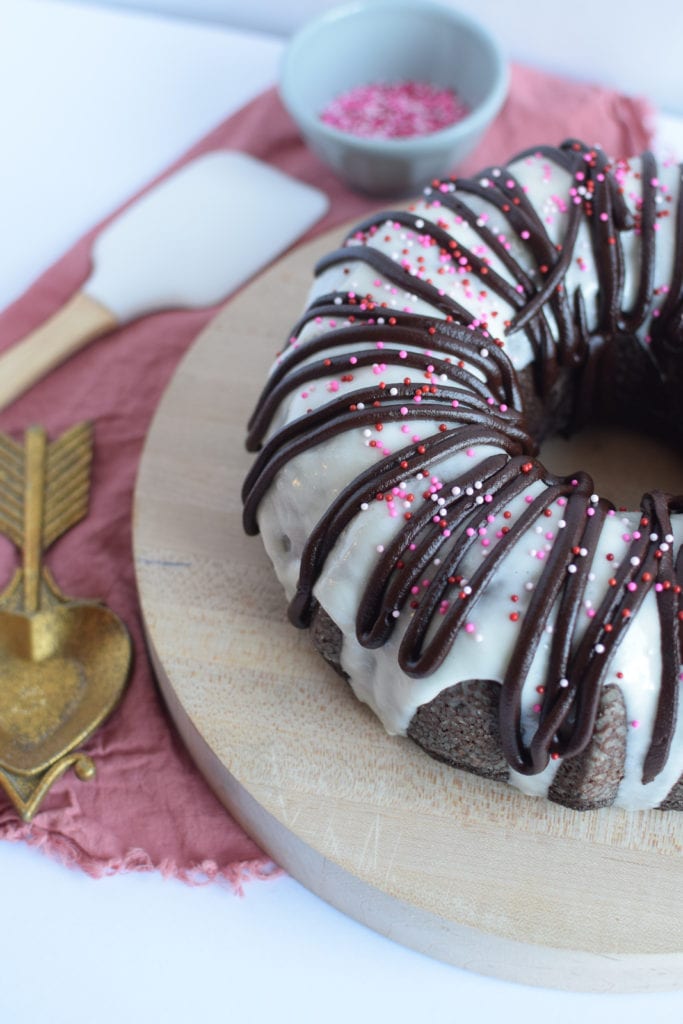 Valentine's chocolate bundt cake covered in vanilla icing and festive sprinkles.