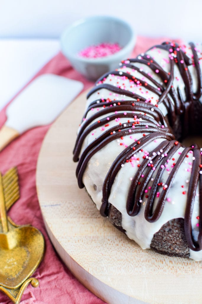 Beautiful chocolate bundt cake covered in vanilla icing and valentine's sprinkles.