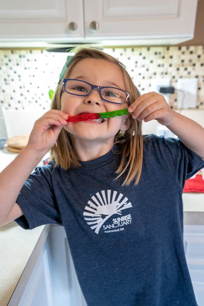 Child eating gummy worm in kitchen.