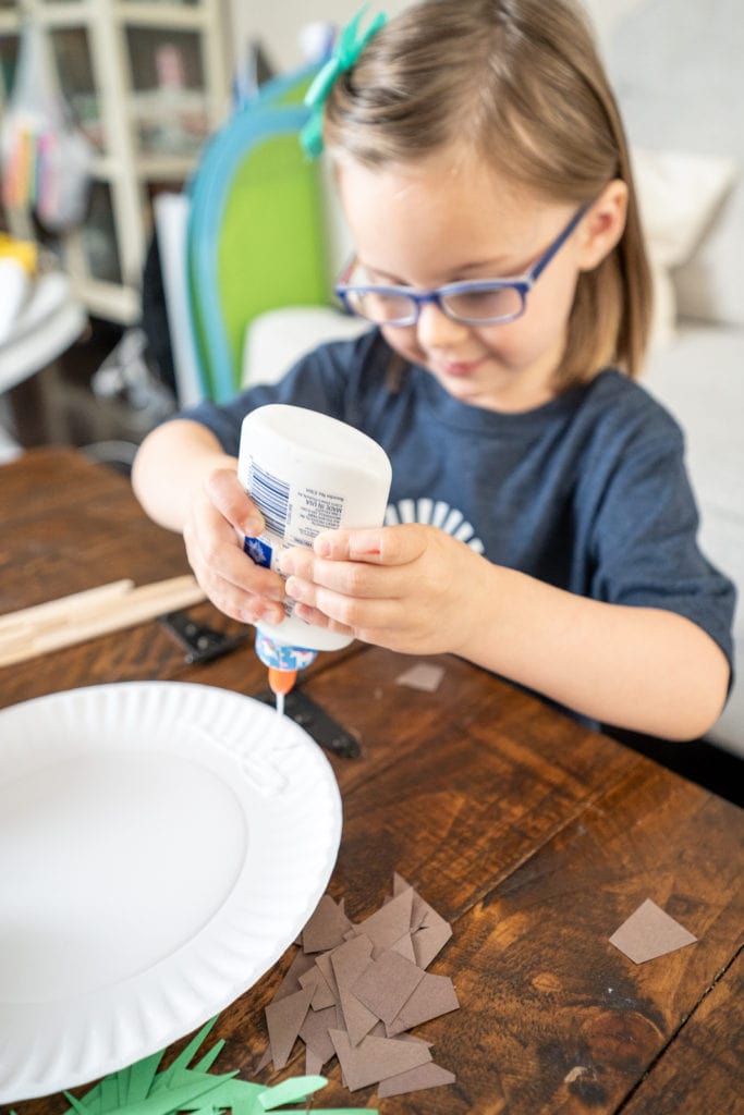 Child gluing items to plate while making craft.