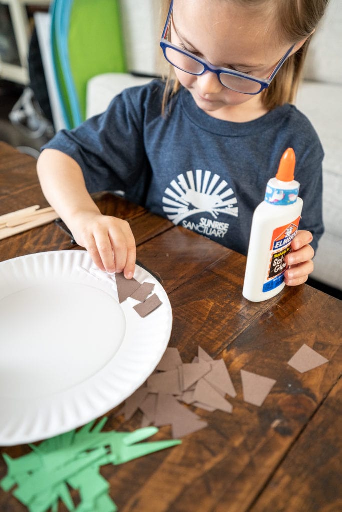 Child gluing items to plate while making craft.