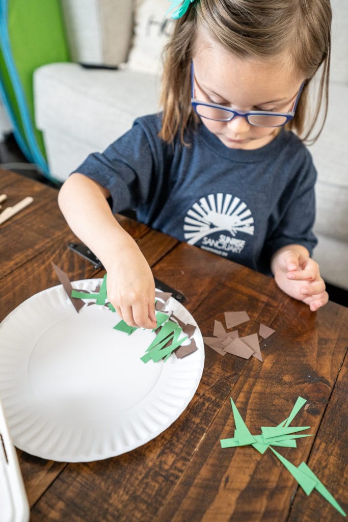 Child gluing additional items to plate while making craft.