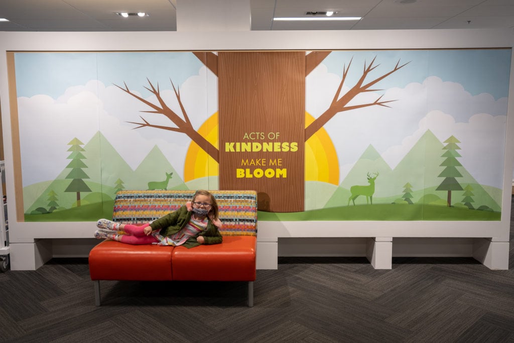 Child in front of acts of kindness make me bloom mural inside library.