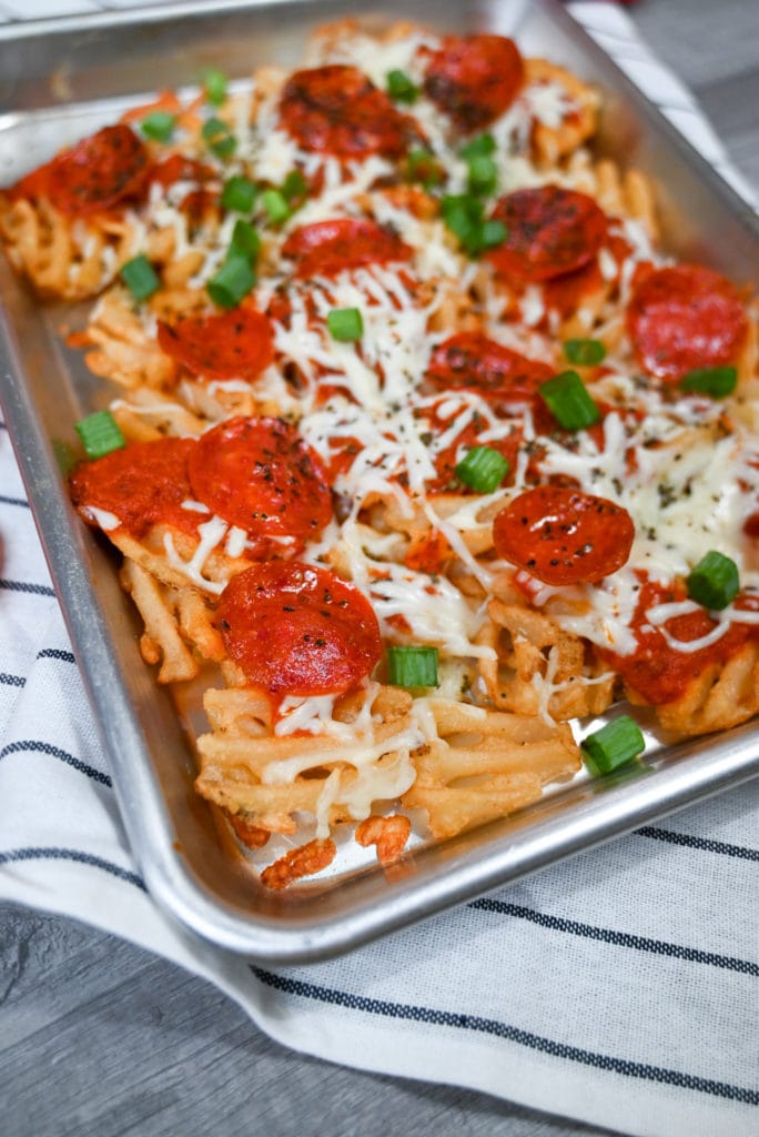 Closeup of a sheet pan full of loaded pizza fries topped with pizza sauce, mozzarella cheese, and sliced pepperonis.