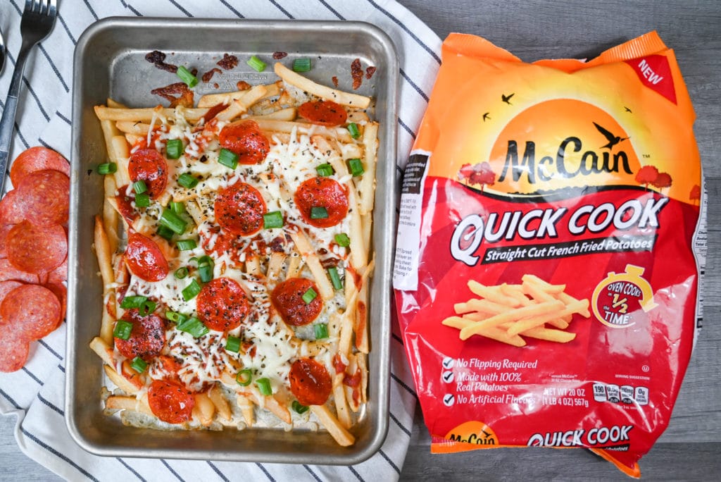 Sheet pan full of finished pizza fries on a decorative towel next to a bag of McCain foods quick cook waffle fries.