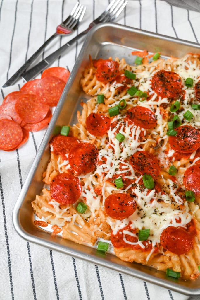 small sheet pan of finished pizza fries garnished with green onions next to forks and sliced pepperoni on a decorative towel.