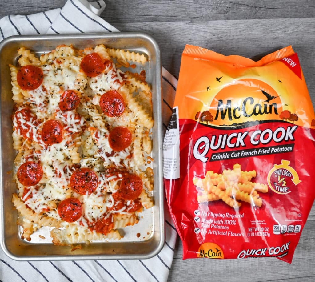 Sheet pan full of finished pizza fries on a decorative towel next to a bag of McCain foods quick cook waffle fries.