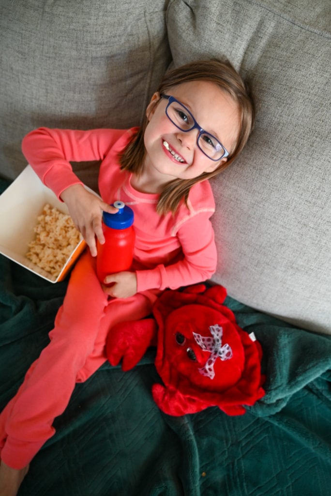 Child enjoying popcorn while wearing pact pajamas on the couch.