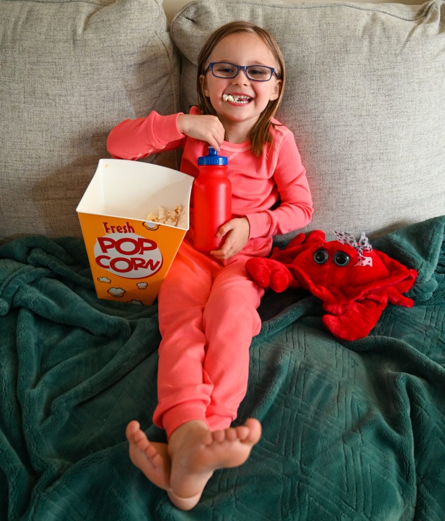 Child enjoying popcorn while wearing pact pajamas on the couch.