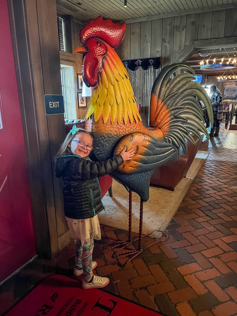 Child posing with large rooster sculpture at the entrance to The Barn at Rocky Fork Creek in Gahanna, Oh.
