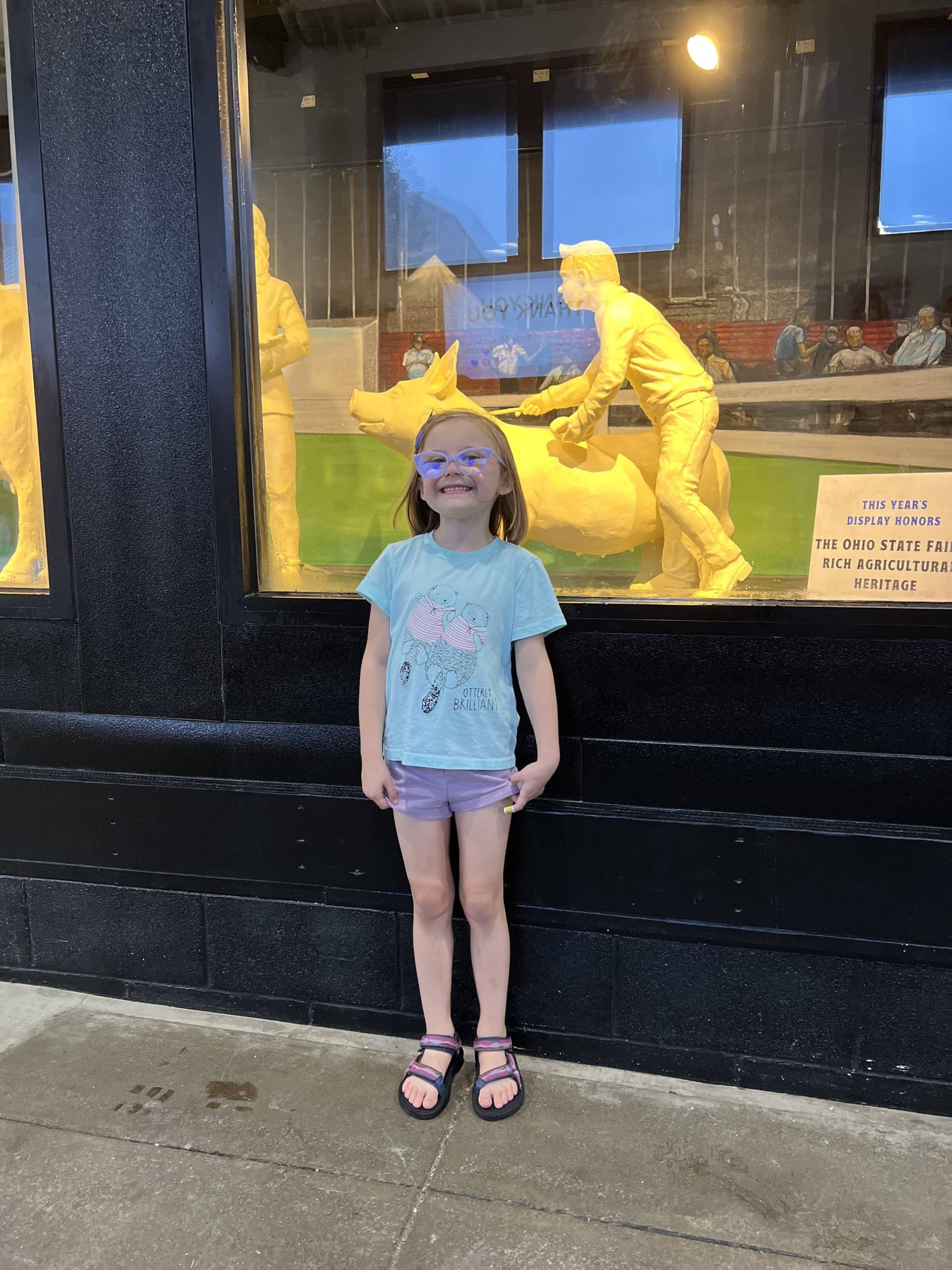 Child posing with the Butter cow and sculptures at The Ohio State Fair.