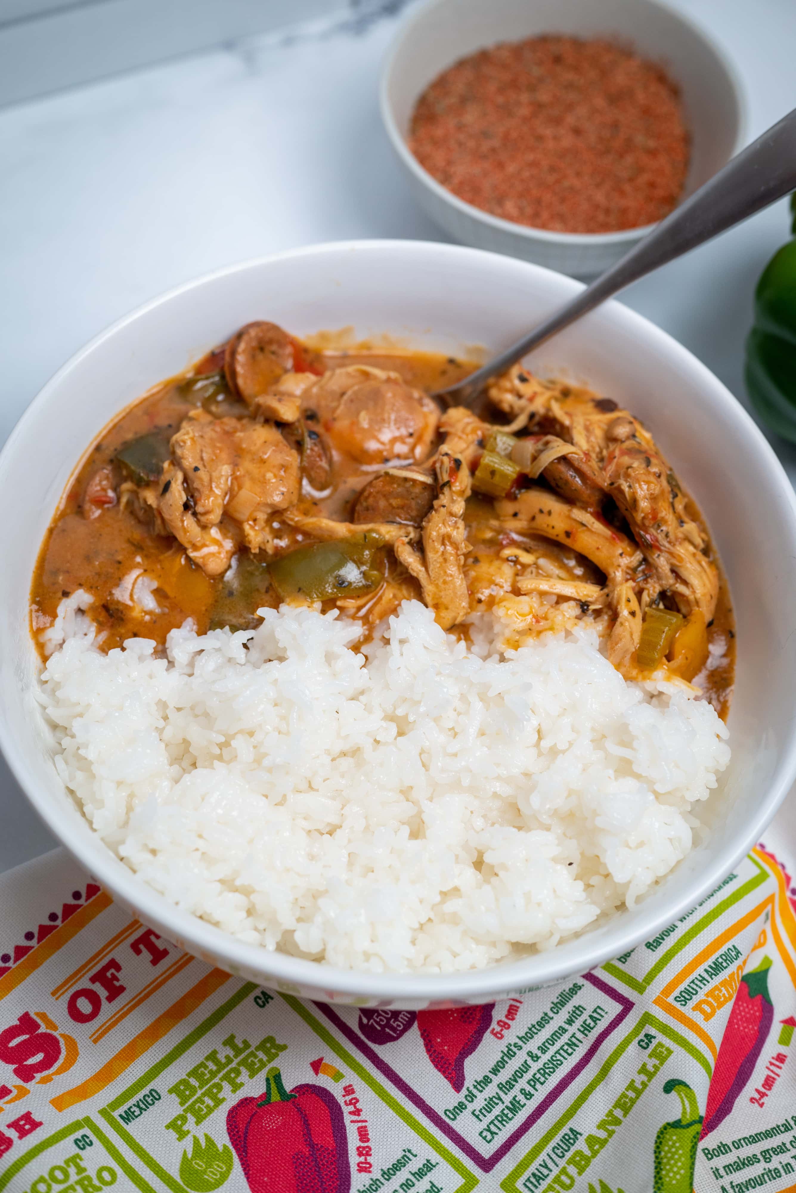 Spicy chicken gumbo served in a bowl with white rice with seasoning blend shown next to bowl.