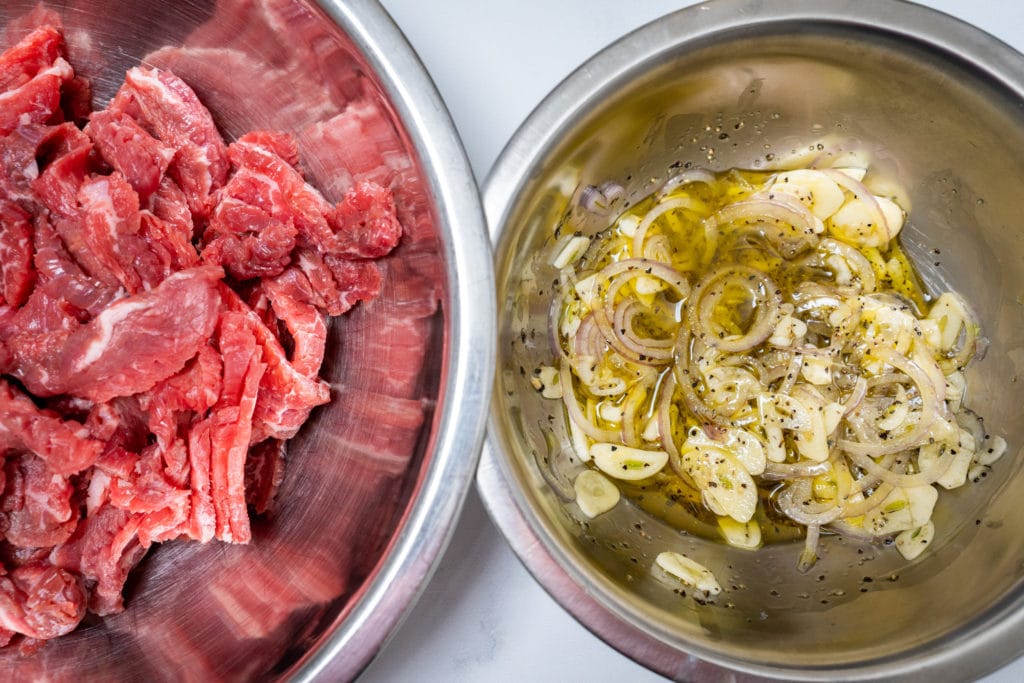 Raw beef in a metal bowl and raw sliced garlic in another metal bowl.