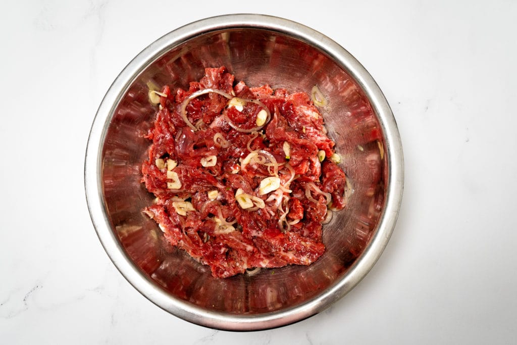 Raw flank steak with garlic in a metal bowl.