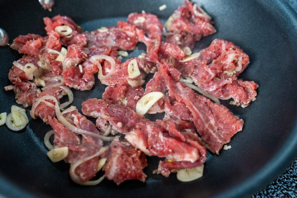 Raw meat and garlic and onions in a pan on the stove. 