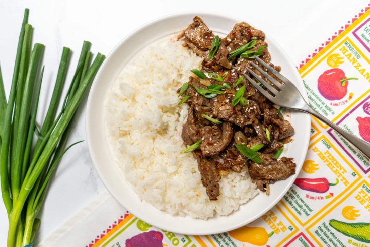 Flank steak stir fry with steamed rice in a white bowl.