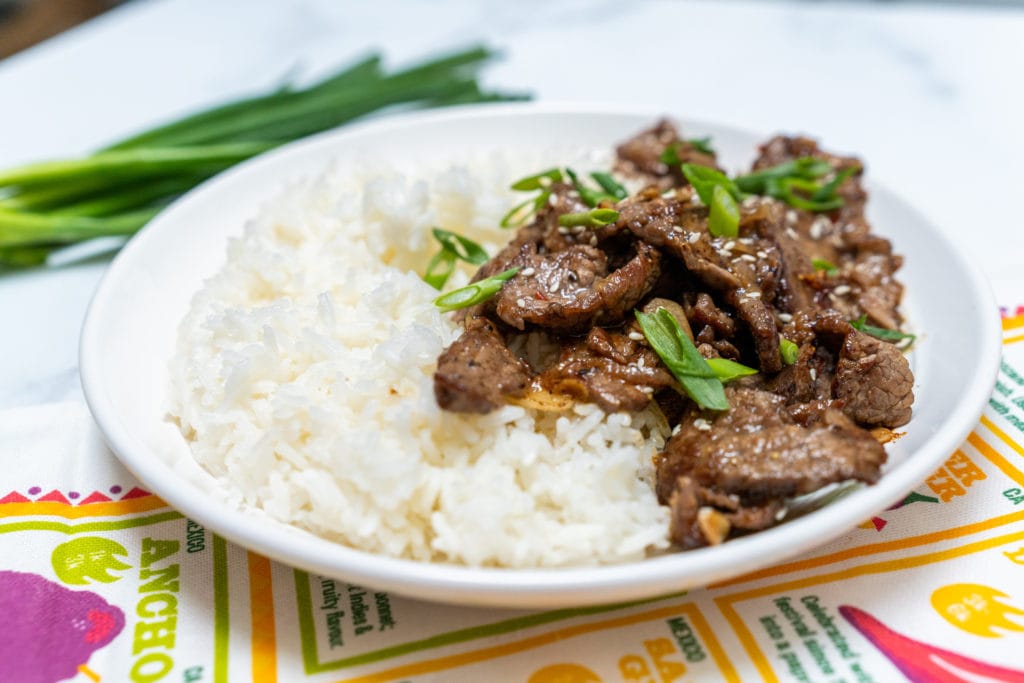 White round plate topped with marinated flank steak and steamed rice. 