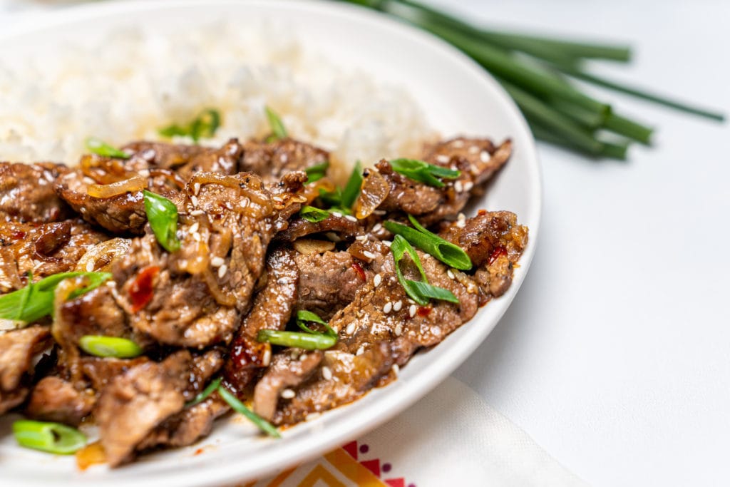 Finished marinated flank steak with steamed white rice and topped with green onions in a white bowl.