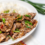 Finished marinated flank steak with steamed white rice and topped with green onions in a white bowl.